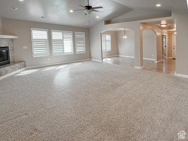 unfurnished living room with light colored carpet, arched walkways, a ceiling fan, baseboards, and a tile fireplace