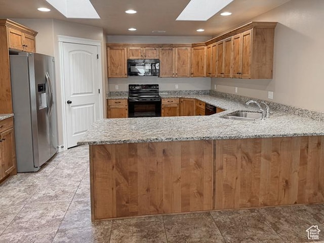 kitchen with a peninsula, a skylight, a sink, and black appliances
