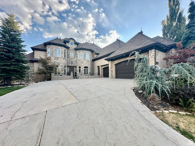 french provincial home featuring an attached garage, concrete driveway, stone siding, and brick siding