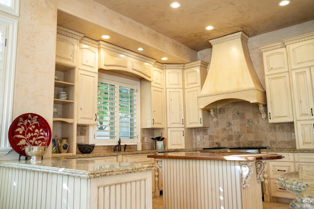 kitchen with stainless steel gas stovetop, recessed lighting, custom exhaust hood, cream cabinets, and backsplash