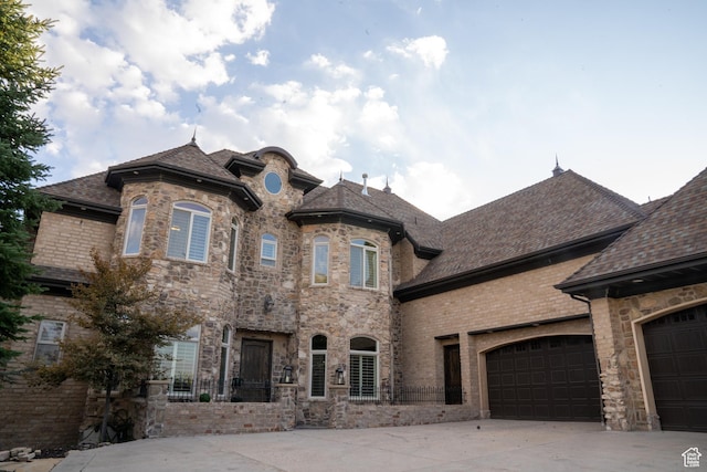 french country home featuring a garage, roof with shingles, driveway, and stone siding
