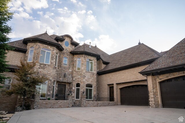 french provincial home with roof with shingles, driveway, and an attached garage