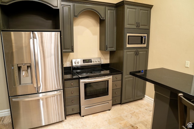 kitchen with stone finish flooring, baseboards, dark countertops, and stainless steel appliances