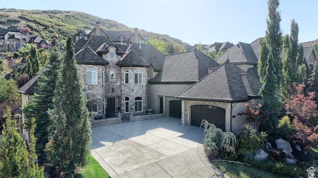 french country inspired facade with a garage, driveway, and stone siding