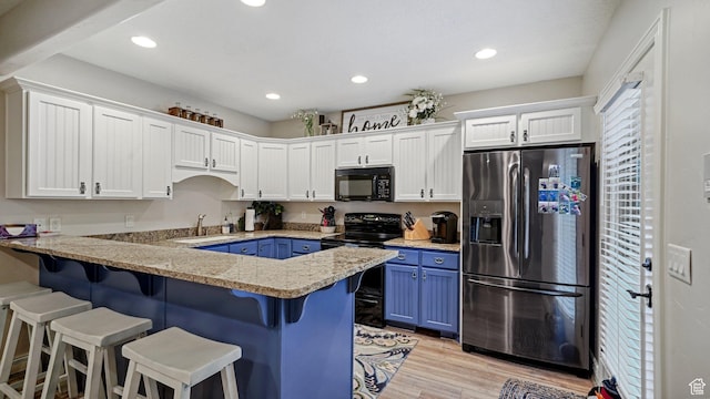 kitchen with a breakfast bar, blue cabinets, white cabinetry, a peninsula, and black appliances