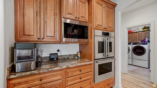 kitchen with stainless steel appliances, brown cabinetry, dark stone counters, separate washer and dryer, and light wood-style floors