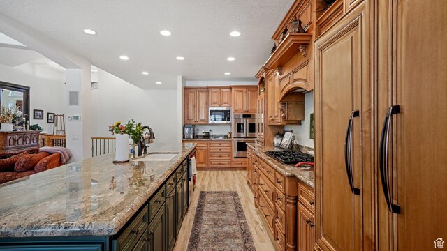 kitchen with light wood-style flooring, a sink, built in appliances, a spacious island, and recessed lighting
