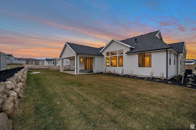 731 W Sara Dr, Saratoga Springs, UT 84045 - back of house at dusk with a patio area, a yard, a shingled roof, central AC unit, and stucco siding