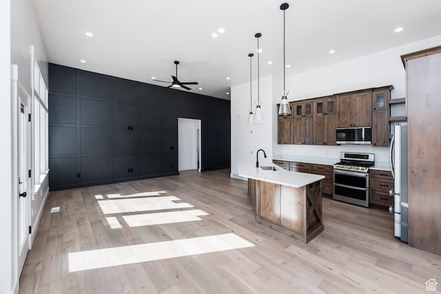 110 S 950 E Unit 45, Hyde Park, UT 84318 - kitchen featuring appliances with stainless steel finishes, pendant lighting, light wood-type flooring, dark brown cabinetry, and a kitchen island with sink