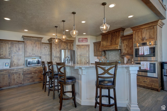 86 Aster Pl, Fish Haven, ID 83287 - kitchen featuring light stone countertops, a large island, stainless steel appliances, decorative light fixtures, and dark hardwood / wood-style floors