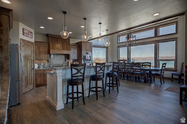 86 Aster Pl, Fish Haven, ID 83287 - kitchen featuring appliances with stainless steel finishes, an island with sink, a textured ceiling, decorative light fixtures, and dark hardwood / wood-style floors