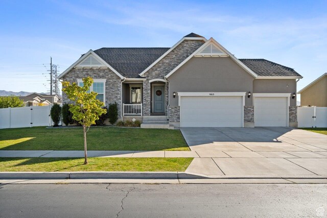 view of front of home featuring driveway, stone siding, an attached garage, a front lawn, and fence