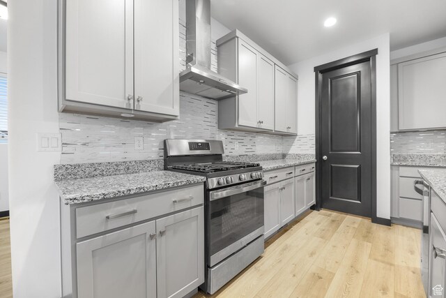 2867 S Greenhead Dr, Saratoga Springs, UT 84045 - kitchen featuring stainless steel gas stove, wall chimney exhaust hood, tasteful backsplash, light wood-type flooring, and light stone counters