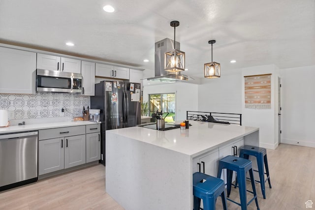 kitchen with tasteful backsplash, island range hood, stainless steel appliances, light wood finished floors, and a kitchen bar
