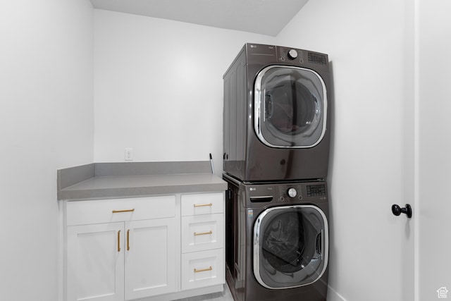 clothes washing area featuring stacked washer / drying machine and cabinet space