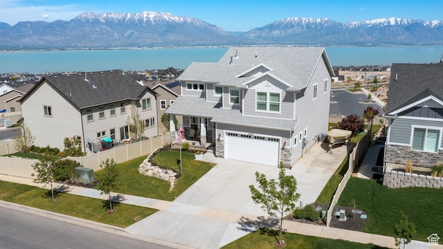 view of front facade with a garage, a water and mountain view, stone siding, concrete driveway, and fence