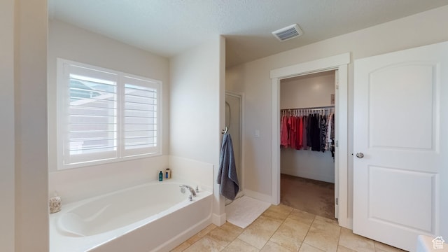 bathroom with a walk in closet, a bath, visible vents, and walk in shower
