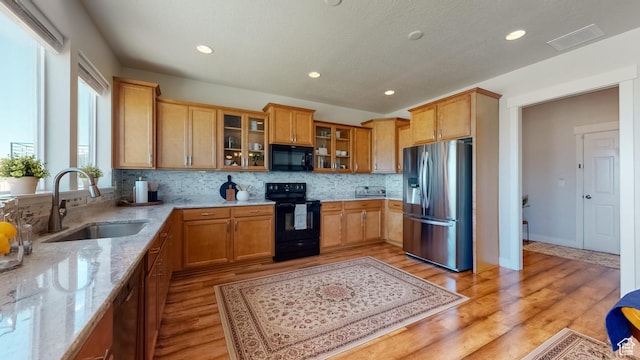 kitchen with tasteful backsplash, a sink, light wood-style floors, black appliances, and light stone countertops