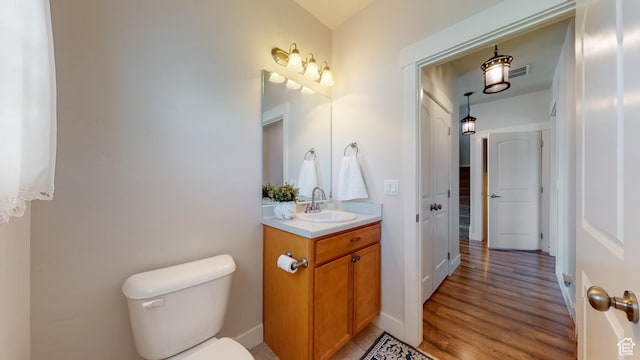 half bathroom with toilet, visible vents, wood finished floors, and vanity