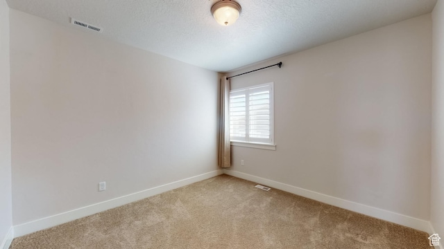 empty room featuring a textured ceiling, visible vents, light colored carpet, and baseboards
