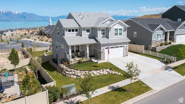 traditional home with concrete driveway, covered porch, an attached garage, fence, and a water and mountain view