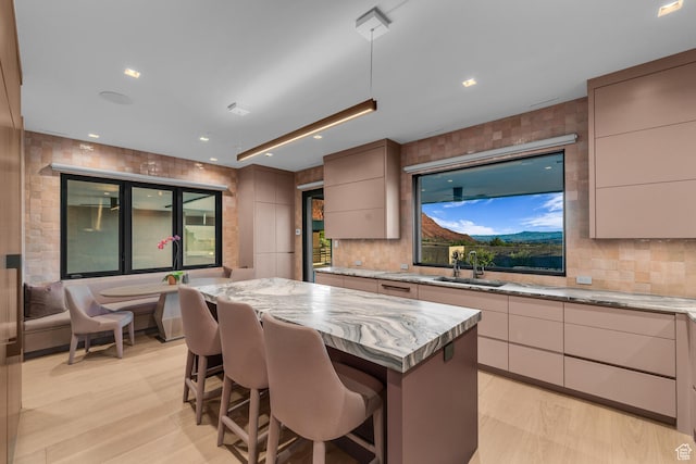 973 W Sipala Trl, Ivins, UT 84738 - kitchen featuring light wood-type flooring, light stone counters, a center island, sink, and backsplash