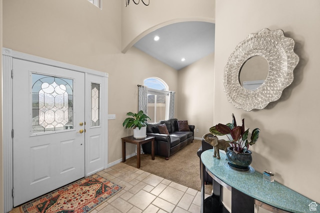 foyer featuring arched walkways, a wealth of natural light, light colored carpet, and a towering ceiling