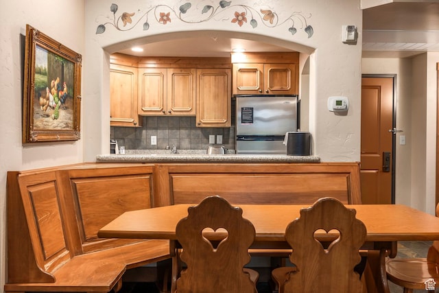 kitchen with freestanding refrigerator, arched walkways, light countertops, brown cabinets, and backsplash