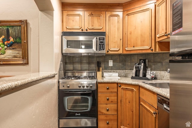 kitchen with appliances with stainless steel finishes, a textured wall, a sink, and backsplash