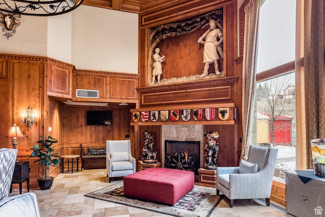 sitting room featuring a towering ceiling, a lit fireplace, wooden walls, visible vents, and stone finish flooring