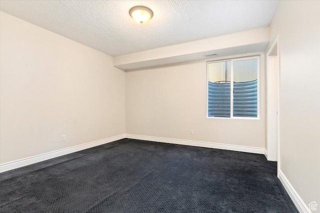spare room with dark carpet, a textured ceiling, and baseboards