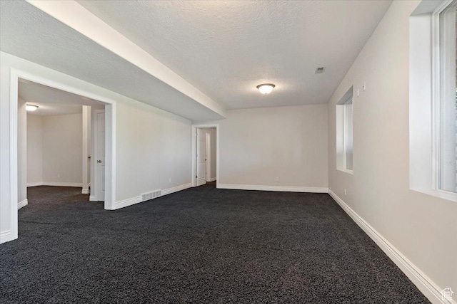 unfurnished room featuring dark colored carpet, a textured ceiling, visible vents, and baseboards