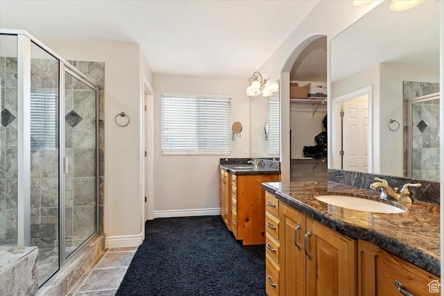 bathroom featuring a sink, a stall shower, two vanities, baseboards, and a spacious closet