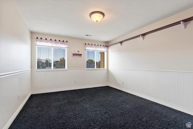 empty room featuring a textured ceiling, visible vents, wainscoting, and dark colored carpet