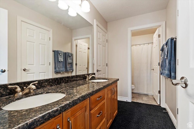 bathroom with baseboards, toilet, double vanity, and a sink