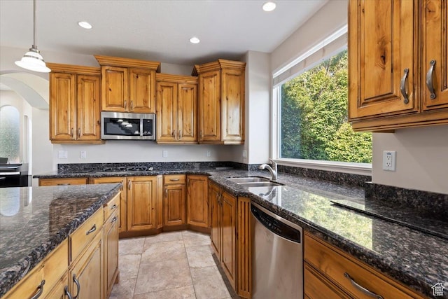 kitchen with dark stone countertops, brown cabinetry, a sink, and stainless steel appliances