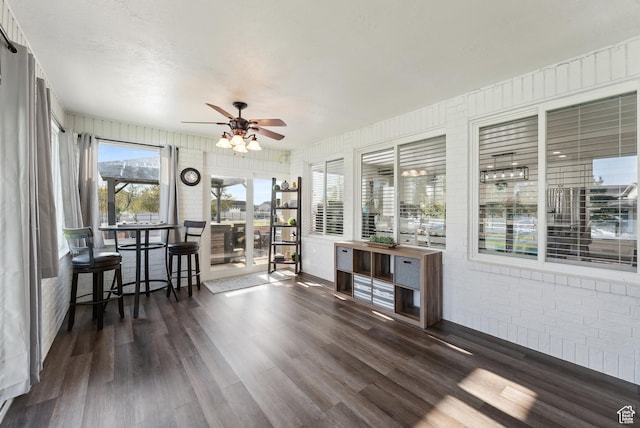 sunroom featuring wood finished floors, ceiling fan, and brick wall