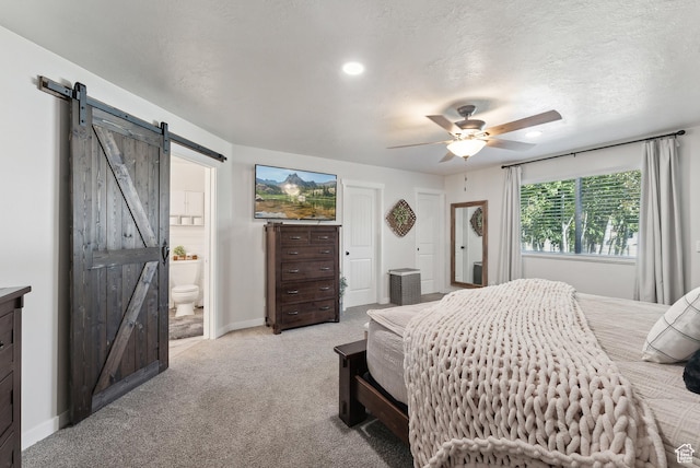 bedroom with connected bathroom, a barn door, light carpet, ceiling fan, and baseboards