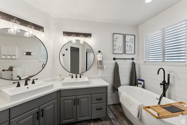 bathroom featuring a soaking tub, wood finished floors, double vanity, and a sink