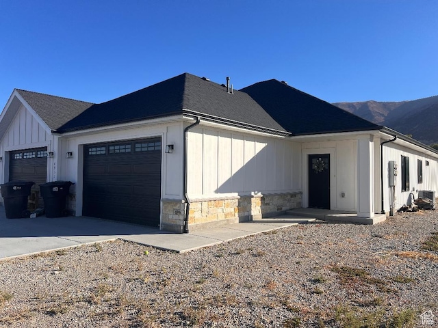 view of home's exterior featuring roof with shingles, a mountain view, stone siding, a garage, and board and batten siding