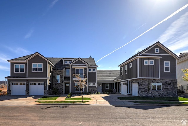 craftsman house with board and batten siding, an attached garage, stone siding, and driveway
