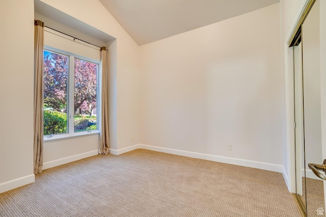 spare room with light carpet, lofted ceiling, and baseboards