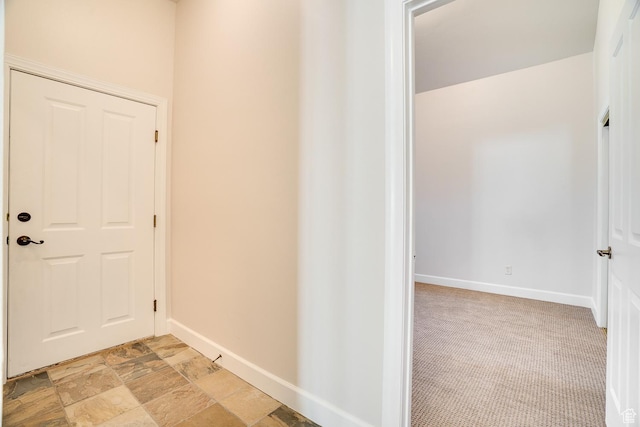 corridor featuring stone finish flooring and baseboards