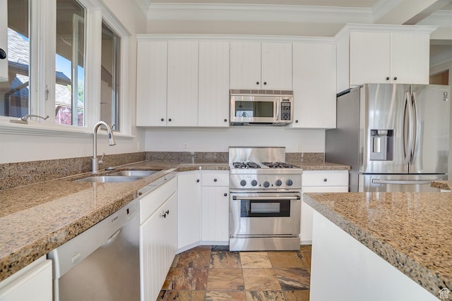 kitchen with stone finish floor, a sink, crown molding, appliances with stainless steel finishes, and white cabinetry