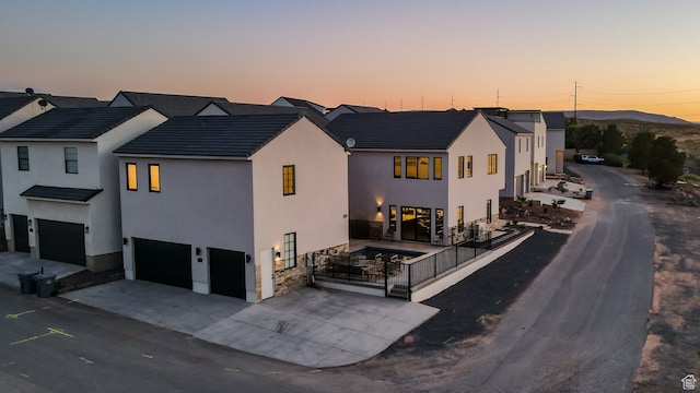 view of front of home featuring a tiled roof, an attached garage, stone siding, stucco siding, and driveway