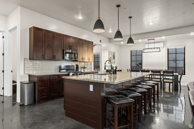 kitchen featuring a sink, stainless steel appliances, a center island with sink, decorative backsplash, and a breakfast bar area