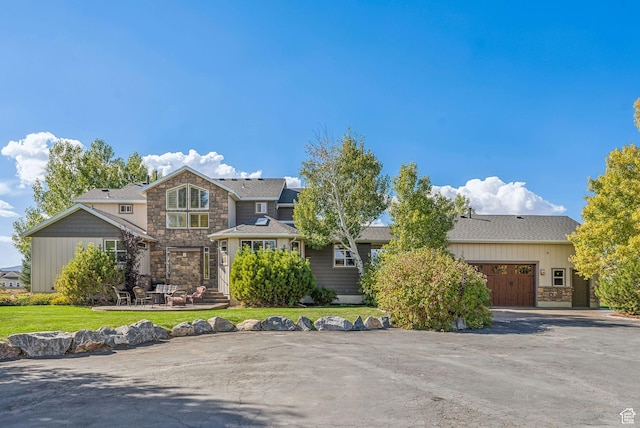 view of front of property featuring a front yard, stone siding, and an attached garage
