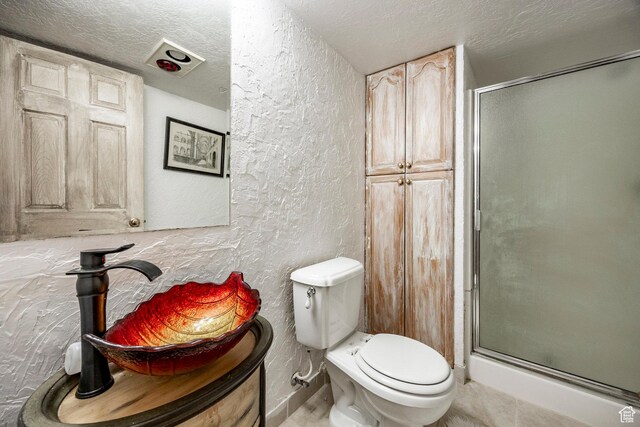 full bath with a textured wall, a stall shower, toilet, and a textured ceiling