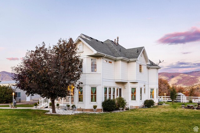 property exterior at dusk with a lawn, a mountain view, and fence