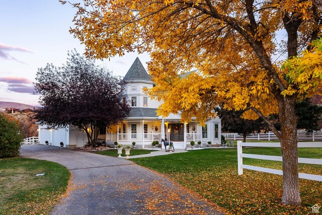 victorian house featuring fence, a shingled roof, a garage, a front yard, and covered porch